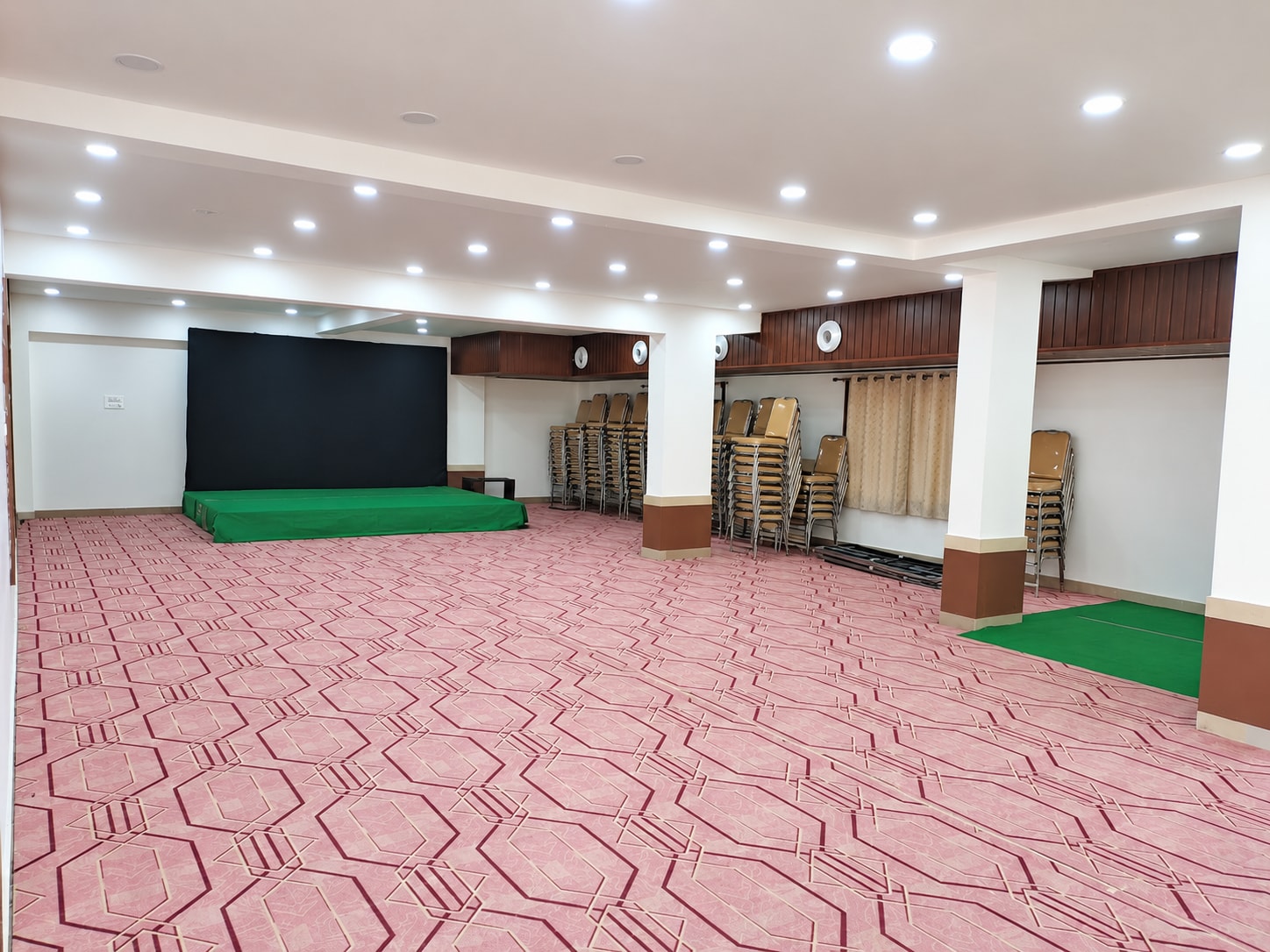 banquet hall floor with a stage, black backdrop and stacked chairs