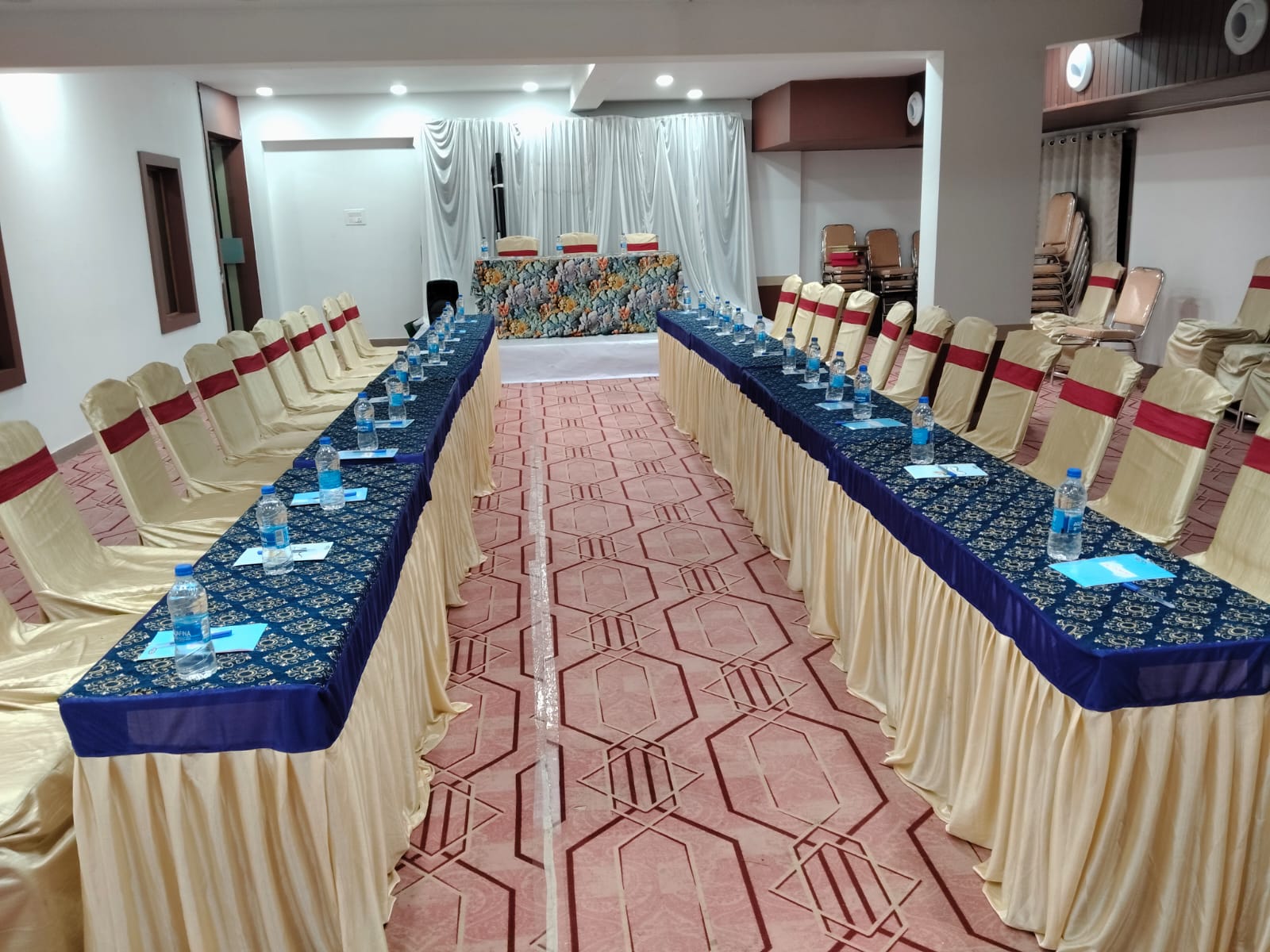 banquet hall set up with draped tables, gold chair covers and a white stage backdrop