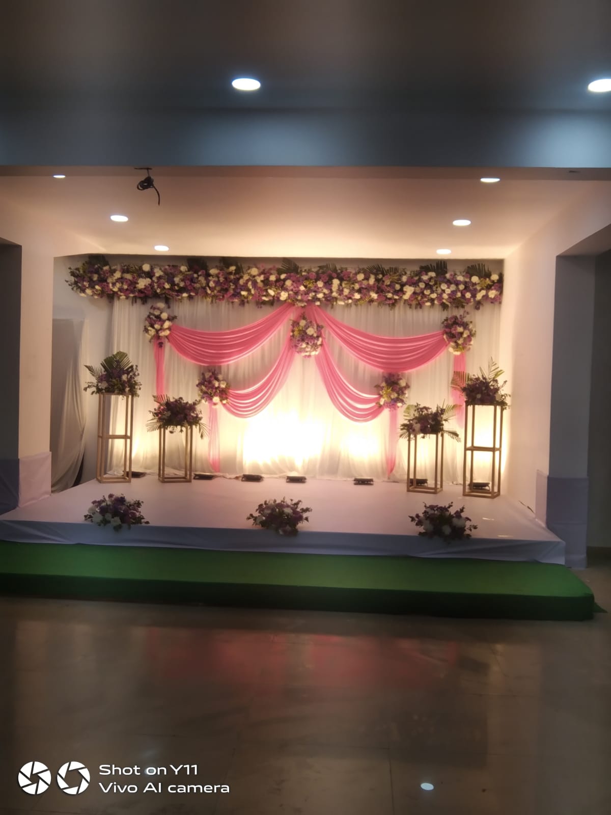 stage with pink drapes and purple and white floral decor, evening lighting